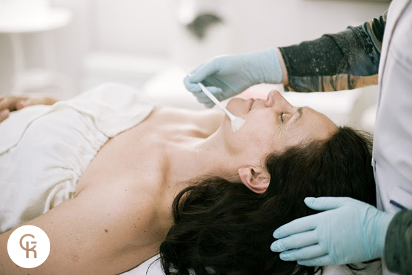 Kobieta podczas nakładania pędzelkiem przez kosmetologa peelingu chemicznego Ferulac Peel